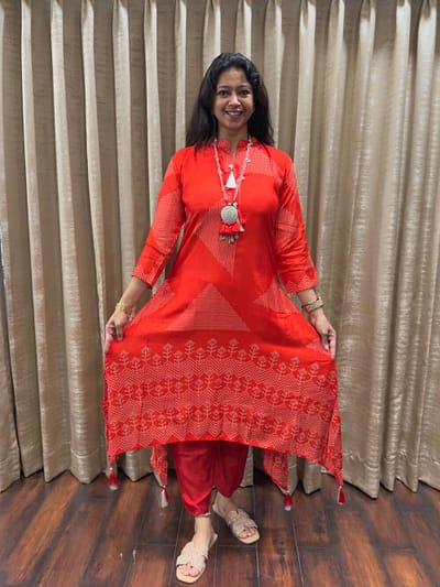 Vermillion red flowy satin silk fabric with high low hemline tasseled edges dotted geometric & floral motifs  Tapered straight pants